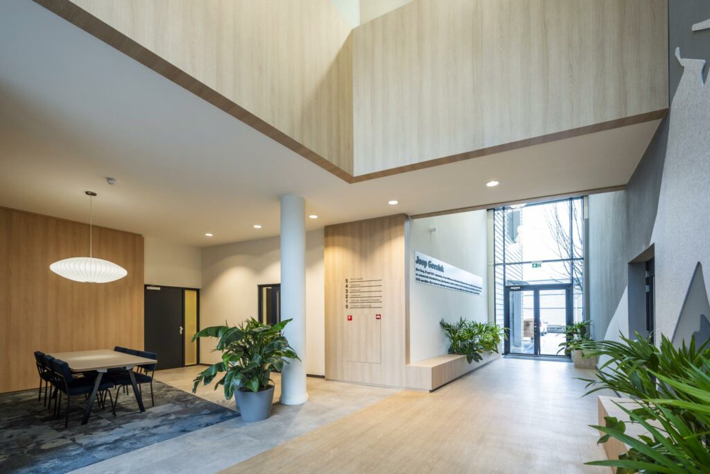 Moderne entreehal van een kantoorgebouw aan de Joop Geesinkweg met houtaccenten, veel daglicht en kamerplanten.